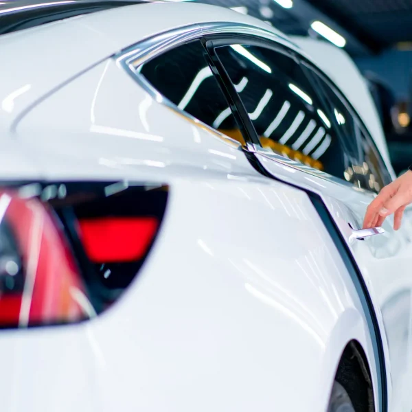 A man opens the door of his luxury white car after detailing and dry cleaning in a car service car rear view White Tesla Model Y back profile with dark window tinting and a man opening the door